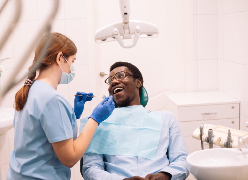 Portrait of young black male patient getting teeth treatment with dentist. professional stomatologist female using dental drill tool for young man.