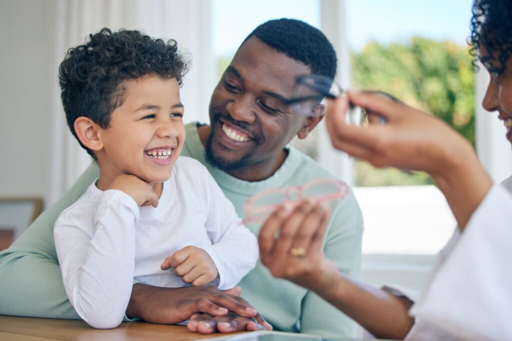 Happy child, glasses choice and father in a doctor office for vision and eye exam with pediatrician. Happiness, dad and young boy together at a clinic looking and lens and frames after a eyes test